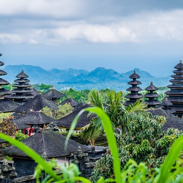 Scenic view of traditional Balinese temples surrounded by lush greenery and mountains under a cloudy sky in Bali, Indonesia.
