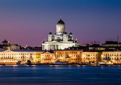 Helsinki Cathedral illuminated at dusk, overlooking the waterfront with historic buildings in the foreground.