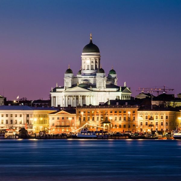 Helsinki Cathedral illuminated at dusk, overlooking the waterfront with historic buildings in the foreground.