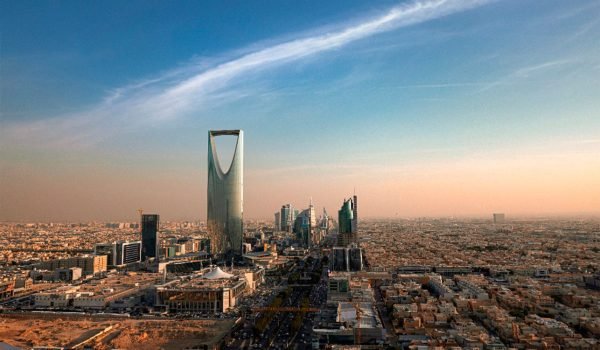 Aerial view of Riyadh, Saudi Arabia, showcasing the iconic Kingdom Centre Tower and modern skyline against a clear blue sky.