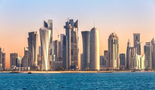 Panoramic view of Doha's skyline at sunset, showcasing modern skyscrapers and architectural landmarks along the waterfront.