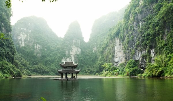 Serene landscape featuring a traditional pavilion on a tranquil lake, surrounded by towering green cliffs and misty mountains, showcasing the beauty of nature.