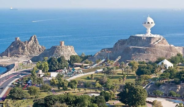 Aerial view of a coastal landscape featuring rocky formations, a lighthouse, and lush greenery along the shoreline, with the ocean in the background.