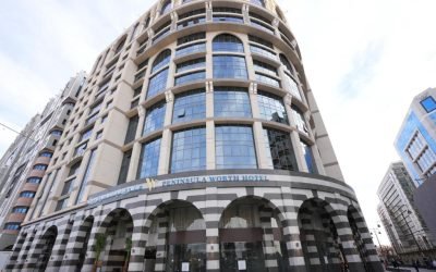Exterior view of the Peninsula Worth Hotel featuring modern architectural design, large glass windows, and distinctive striped columns, located in a bustling urban setting. Ideal for travelers seeking luxury accommodations.