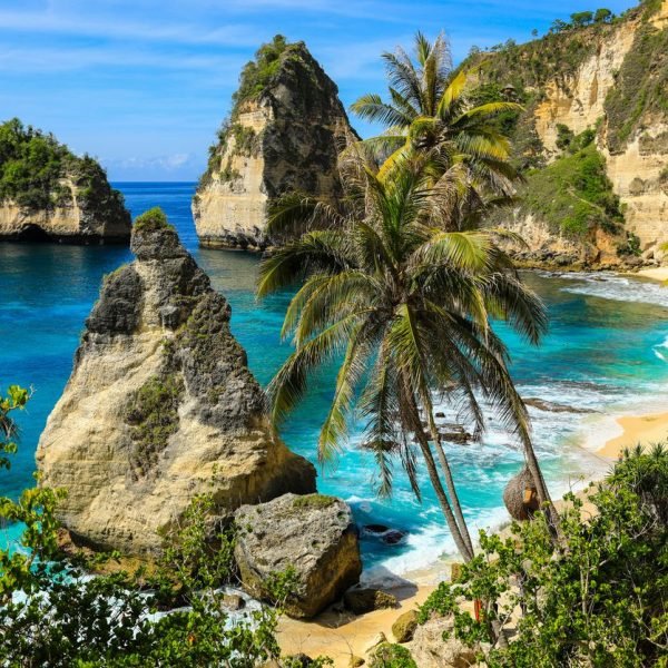 Stunning tropical beach with turquoise waters, palm trees, and rocky cliffs, showcasing a serene coastal landscape in a sunny environment.