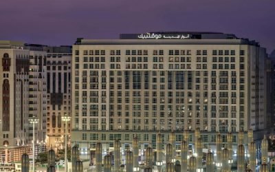 Modern hotel building in Medina, Saudi Arabia, featuring illuminated architectural details and surrounded by decorative columns at dusk.