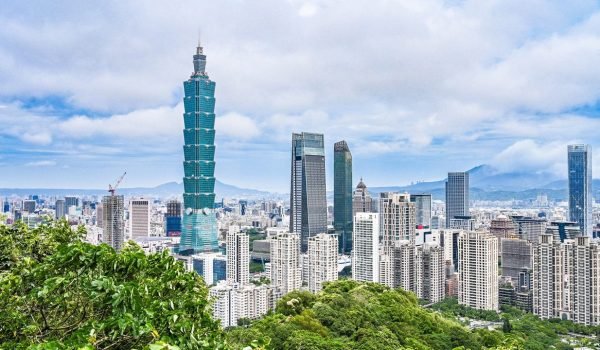 Taipei skyline featuring Taipei 101 tower surrounded by modern skyscrapers and lush greenery under a cloudy sky.