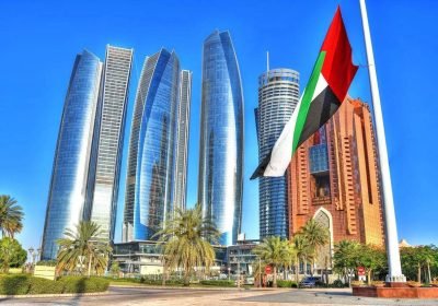 Modern skyscrapers in Abu Dhabi with the UAE flag in the foreground, showcasing the city's architectural advancements and vibrant atmosphere.