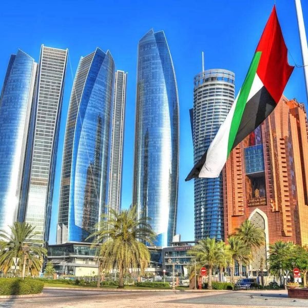 Modern skyscrapers in Abu Dhabi with the UAE flag in the foreground, showcasing the city's architectural advancements and vibrant atmosphere.
