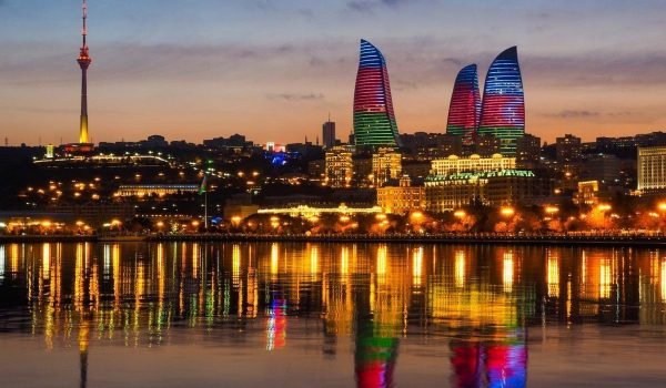 Baku skyline at sunset showcasing the Flame Towers illuminated with colorful lights, reflecting in the water, highlighting the city's modern architecture and vibrant nightlife.