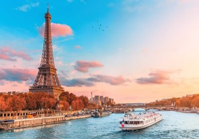 Eiffel Tower at sunset, with a scenic view of the Seine River and a boat cruising along the water, showcasing Paris's iconic landscape.