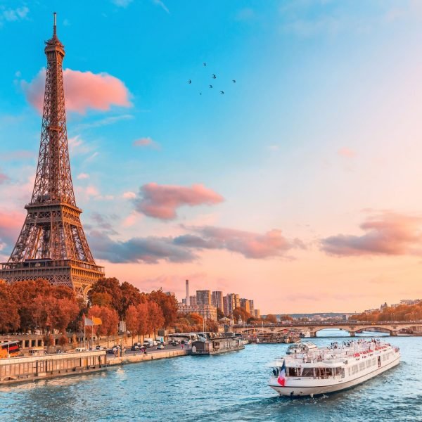 Eiffel Tower at sunset, with a scenic view of the Seine River and a boat cruising along the water, showcasing Paris's iconic landscape.