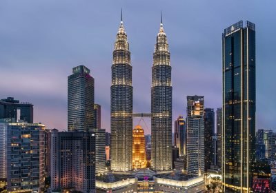 Skyline view of the Petronas Twin Towers in Kuala Lumpur, Malaysia, illuminated at dusk, surrounded by modern skyscrapers.