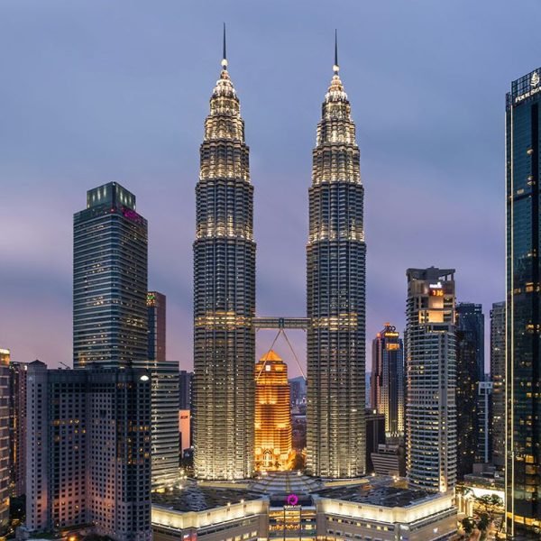 Skyline view of the Petronas Twin Towers in Kuala Lumpur, Malaysia, illuminated at dusk, surrounded by modern skyscrapers.
