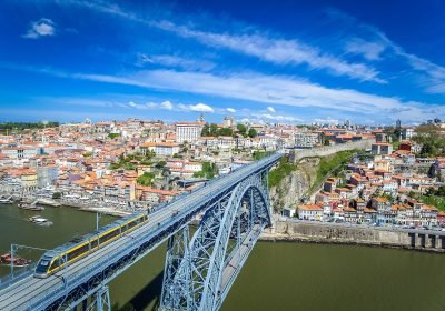 Aerial view of the Dom Luís I Bridge in Porto, Portugal, showcasing the city's colorful buildings and the Douro River under a clear blue sky.
