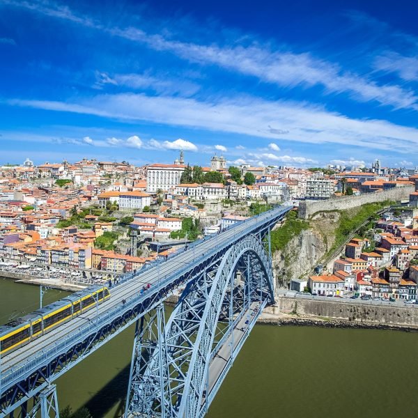 Aerial view of the Dom Luís I Bridge in Porto, Portugal, showcasing the city's colorful buildings and the Douro River under a clear blue sky.