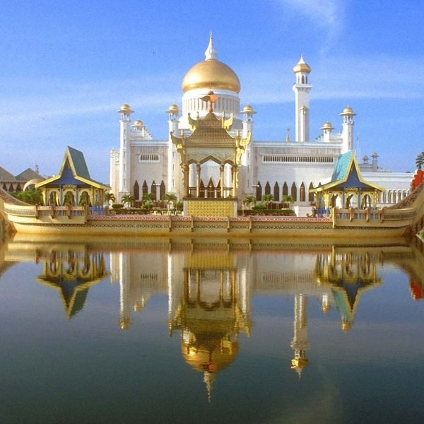 Majestic view of the Sultan Omar Ali Saifuddien Mosque in Brunei, featuring its stunning golden dome and intricate architecture reflected in the serene water, under a clear blue sky.