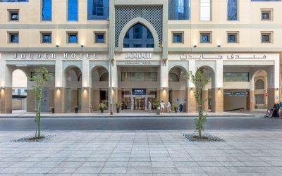 Front view of Jayden Hotel showcasing its modern architecture, entrance with arched columns, and signage in both English and Arabic, with pedestrians walking along the street.