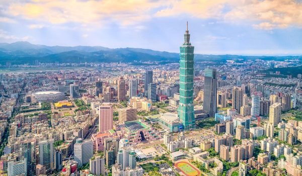 Aerial view of Taipei, Taiwan, showcasing the iconic Taipei 101 skyscraper surrounded by a bustling urban landscape and mountains in the background.