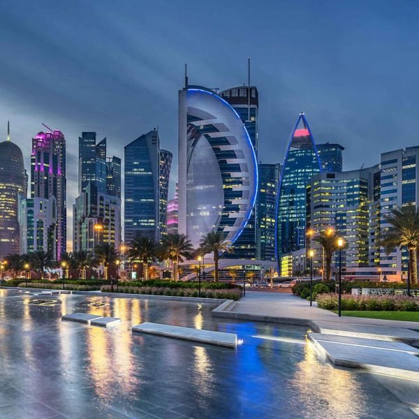 Cityscape of Doha, Qatar, showcasing modern skyscrapers illuminated at dusk, with the iconic Aspire Tower in the foreground and reflections on the water.