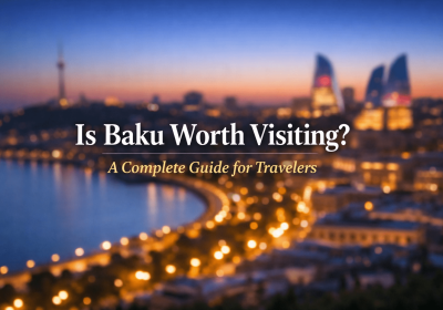 Cityscape of Baku, Azerbaijan at dusk featuring illuminated buildings along the waterfront, with the text overlay "Is Baku Worth Visiting? A Complete Guide for Travelers."