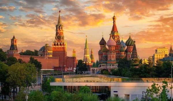 View of the Kremlin and St. Basil's Cathedral in Moscow at sunset, showcasing iconic Russian architecture against a colorful sky.