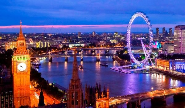Aerial view of the London skyline at dusk featuring the illuminated London Eye, the River Thames, and historic architecture, showcasing a vibrant cityscape.