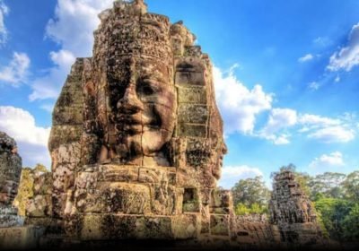 Stone faces of Bayon Temple in Angkor Thom, Cambodia, against a blue sky, showcasing intricate carvings and historical significance.