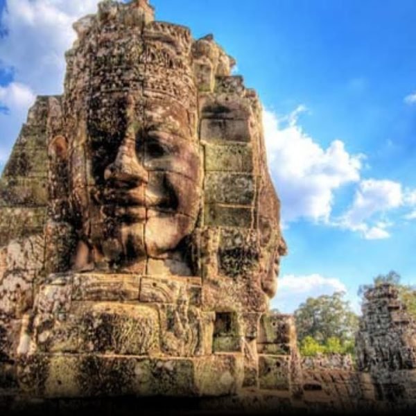Stone faces of Bayon Temple in Angkor Thom, Cambodia, against a blue sky, showcasing intricate carvings and historical significance.