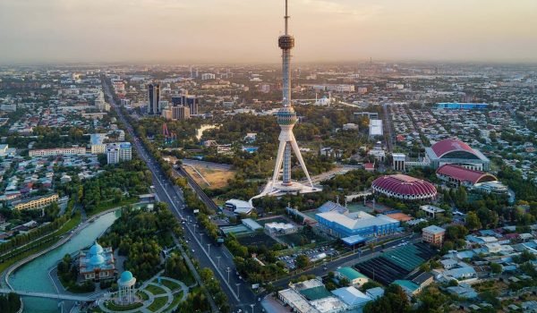 Aerial view of the Tashkent TV Tower surrounded by cityscape and greenery at sunset in Tashkent, Uzbekistan.