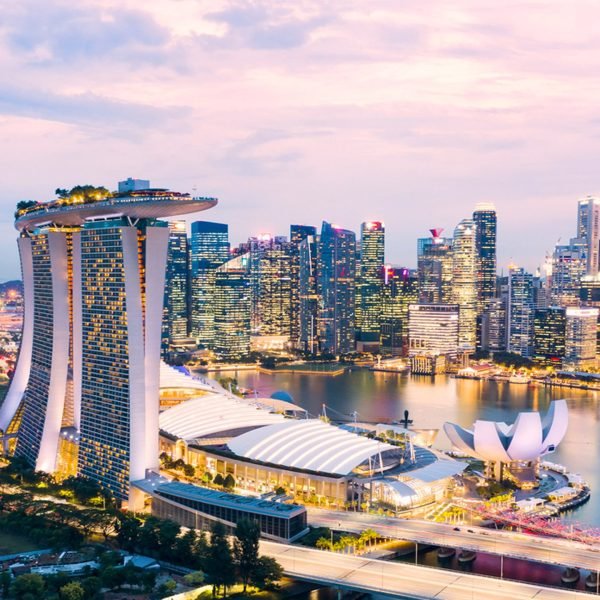 Aerial view of Singapore's Marina Bay area at sunset, featuring the iconic Marina Bay Sands hotel and the futuristic ArtScience Museum, surrounded by a vibrant city skyline.