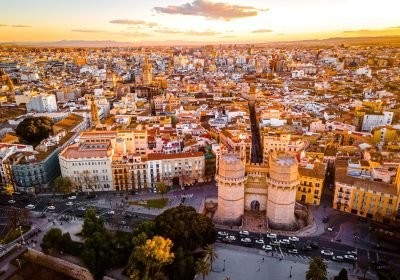 Aerial view of Valencia, Spain, showcasing the historic Torres de Serranos and the vibrant cityscape at sunset, highlighting the blend of modern and traditional architecture.