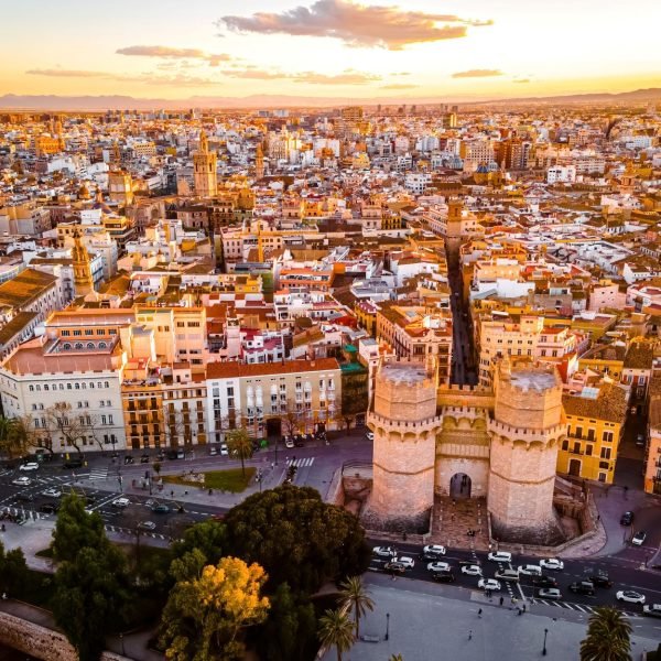 Aerial view of Valencia, Spain, showcasing the historic Torres de Serranos and the vibrant cityscape at sunset, highlighting the blend of modern and traditional architecture.